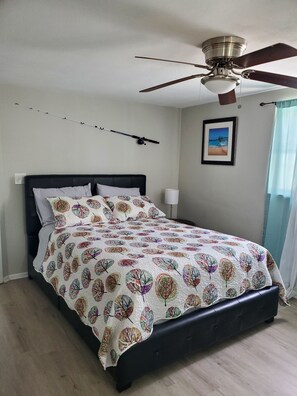 A bedroom with a bed, a ceiling fan, a framed picture on the wall, and a window with curtains.