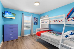 A child’s bedroom with a bunk bed, a dresser, a TV, and a window with curtains.
