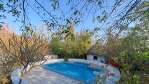 A round swimming pool with a tiled deck, surrounded by trees and a small building with a thatched roof. - Nature Retreat Cottages Jaisamand Udaipur  (Udaipur)