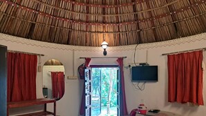 A room with a thatched roof, a television mounted on the wall, and a view of the outdoors through a door. - Nature Retreat Cottages Jaisamand Udaipur  (Udaipur)