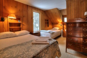 Une chambre confortable, aménagée dans un chalet en bois, avec deux lits, une commode et une fenêtre laissant entrer la lumière naturelle.
