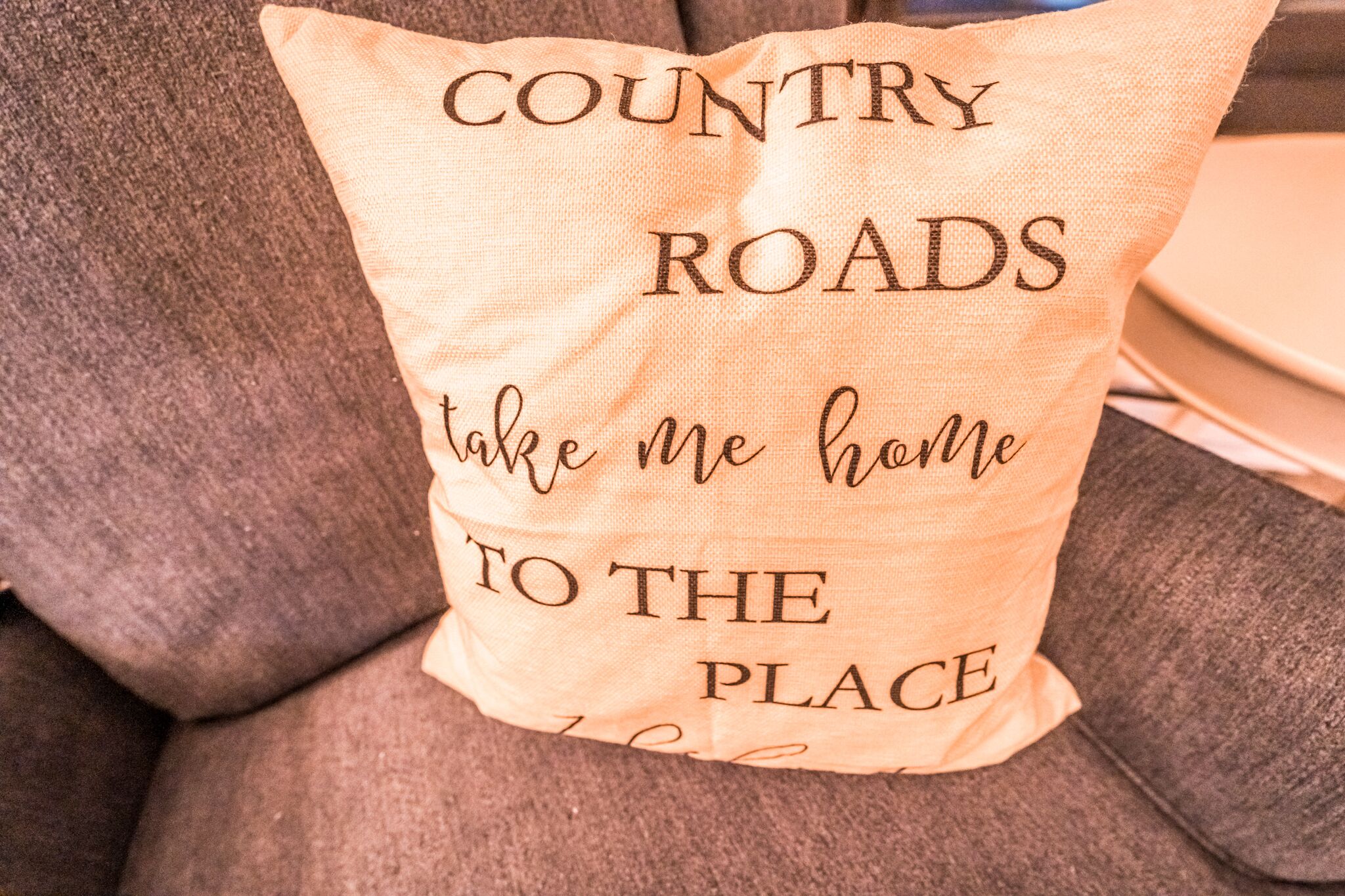 Un coussin orné du texte : « COUNTRY ROADS take me home TO THE PLACE ».
