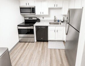 A modern kitchen with stainless steel appliances, white cabinetry, and a wooden floor.