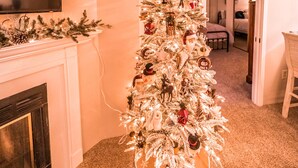 Un arbre de Nadal en un passadís amb una llar de foc, sòl amb moqueta i una zona de menjador al fons.