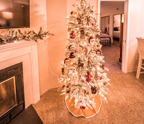 Un sapin de Noël dans un couloir, avec une cheminée, un sol recouvert de moquette et un coin repas à l’arrière-plan.