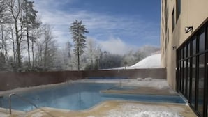 Ein Schwimmbecken, umgeben von Schnee, mit Bäumen im Hintergrund und einem Gebäude mit Fenstern.