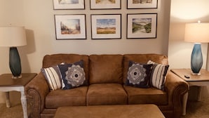 Ein braunes Ledersofa mit dekorativen Kissen, ein passendes Ottomanen und gerahmte Landschaftsbilder an der Wand.