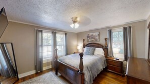 A bedroom with a bed, nightstands, a dresser, a ceiling fan, and a window with curtains.