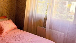 A bedroom with a bed, a radiator, and a window with curtains.