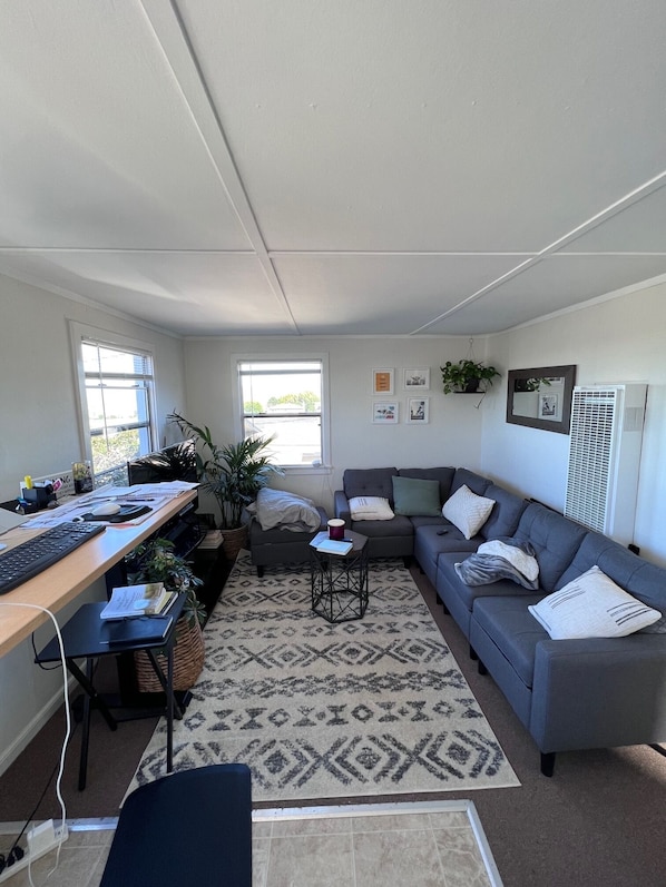A modern living room with a grey sofa, a small coffee table, a desk with a computer, and a patterned rug.
