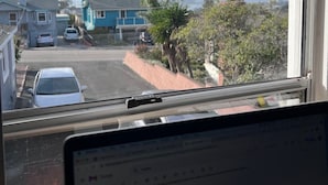 A view from inside a room looking out through a window at a parking lot with several cars, a blue building, and a mountain in the distance. - WFH surfer dream spot in Morro Bay - Looking for a March & April booking (Morro Bay)