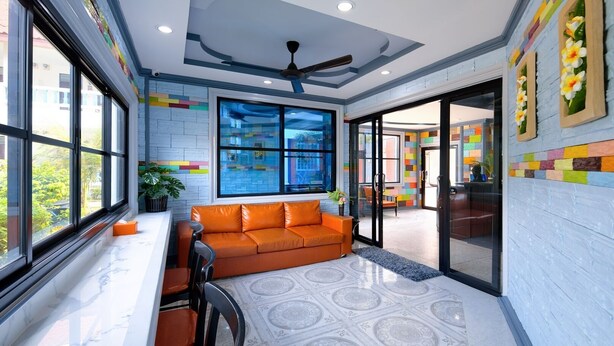 A modern living room with a large window, a ceiling fan, and a colorful wall design. - Kerton Hostel (Koh Samui)