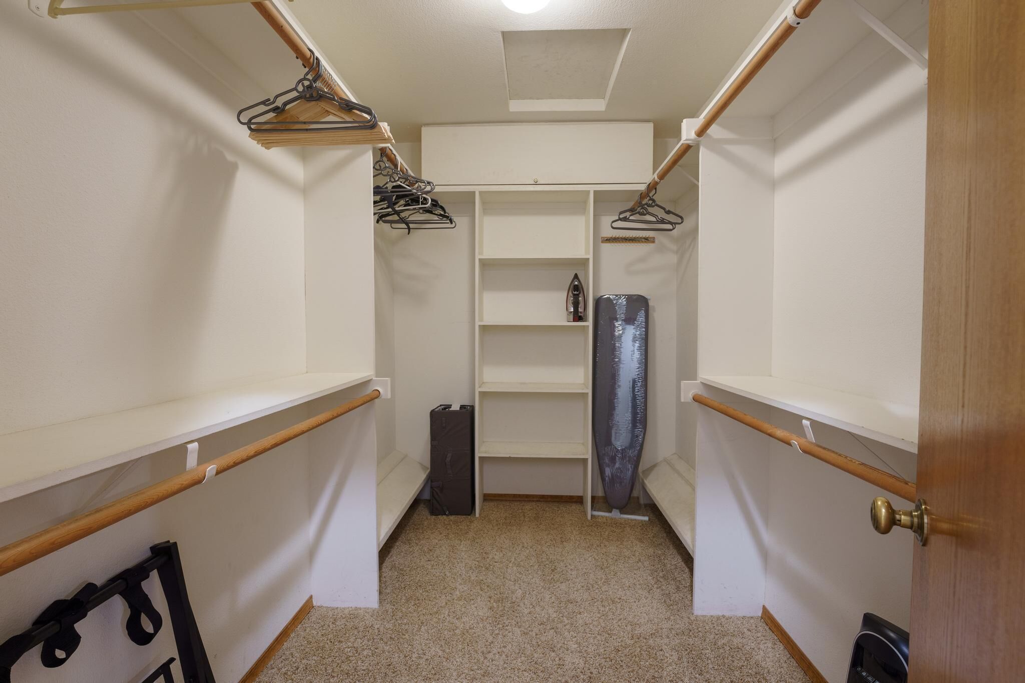 Un petit dressing étroit avec des étagères en bois, des vêtements suspendus et un porte-chaussures.