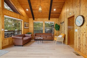 Interno di una baita in legno con un divano in pelle marrone, una sedia in vimini e un tavolo in legno.