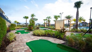 Un campo de mini golf con césped artificial verde, palmeras y un camino de ladrillo.