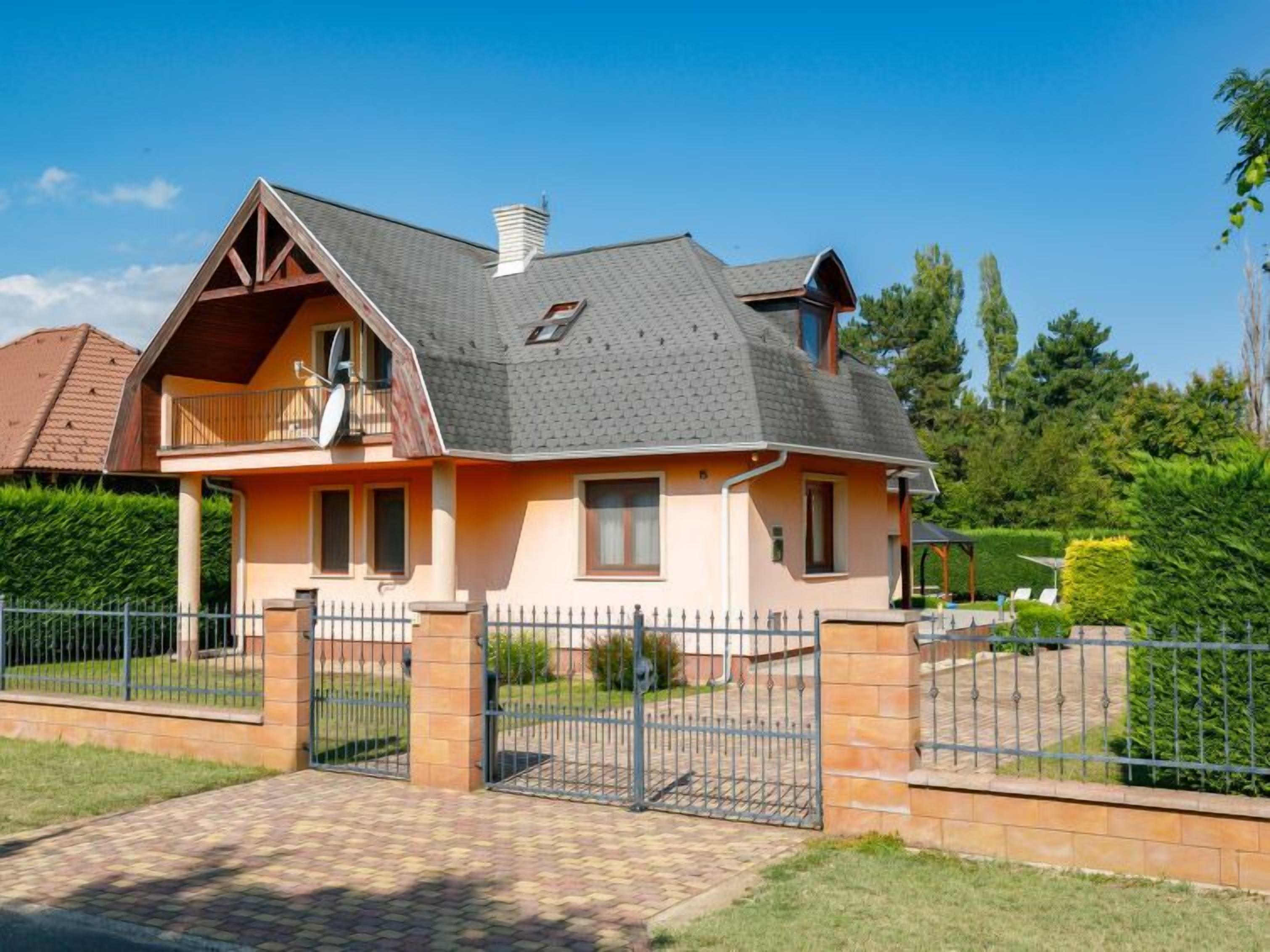 Une maison à deux étages avec un toit en pente, un balcon et une allée menant à une porte grillagée.