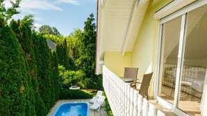 A small pool area with two lounge chairs, surrounded by dense greenery and a white fence. - Vacation home Edina by Interhome (Balatonszarszo)