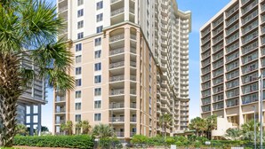 A high-rise residential building with multiple balconies, surrounded by greenery and palm trees. - $150 activities - E-gift card when you book - Southern Ocean View with Gorgeous Sunsets | RP1906-2 (Myrtle Beach)