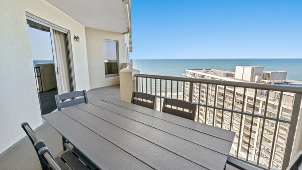 A balcony with a table and chairs, overlooking a beach and a high-rise building. - $150 activities - E-gift card when you book - Southern Ocean View with Gorgeous Sunsets | RP1906-2 (Myrtle Beach)