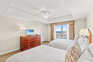 A hotel room with two beds, a ceiling fan, a TV, and a view of the city.