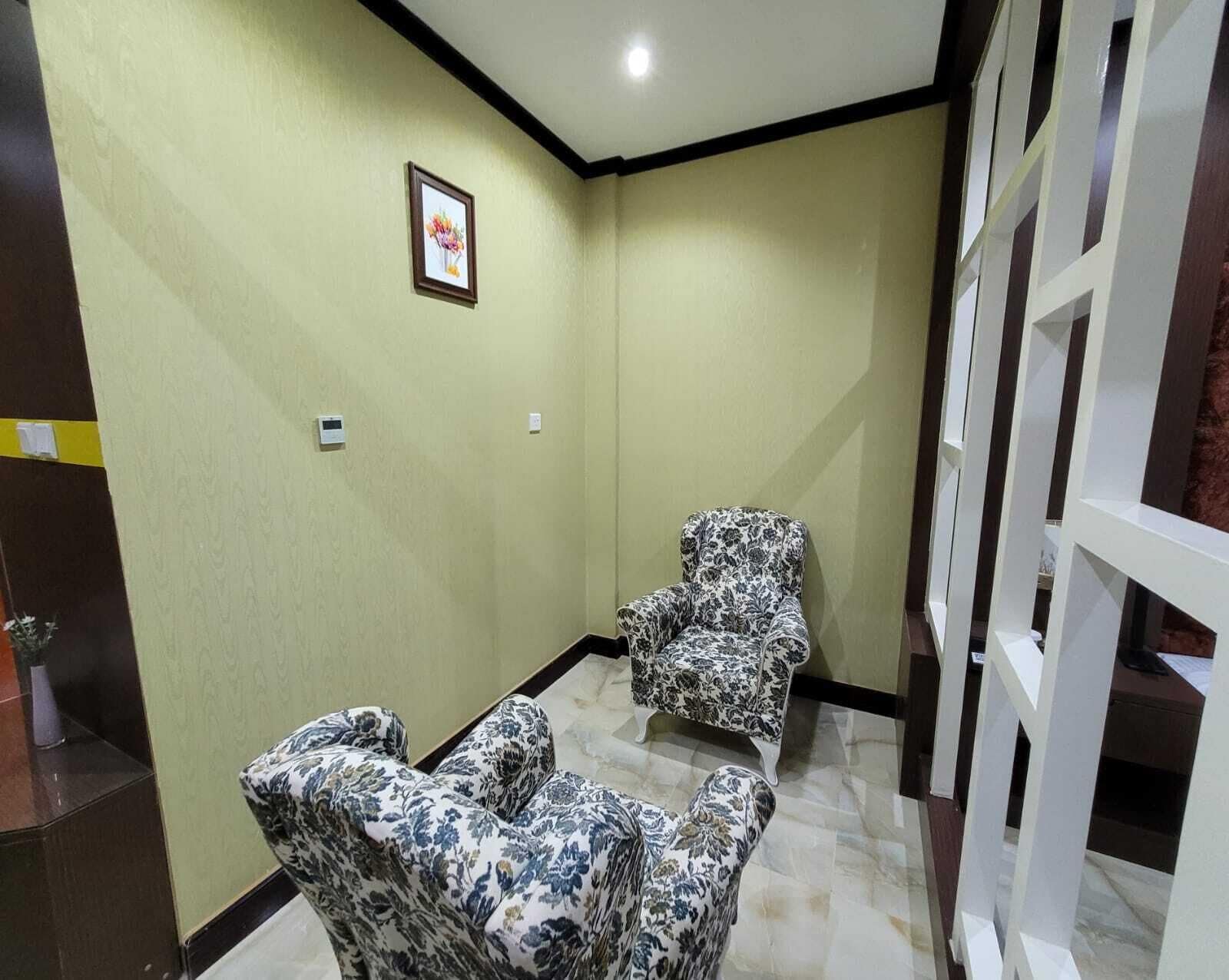 Et værelse med to mønstrede lænestole, et billede i ramme på væggen og en hvid rumdeler.