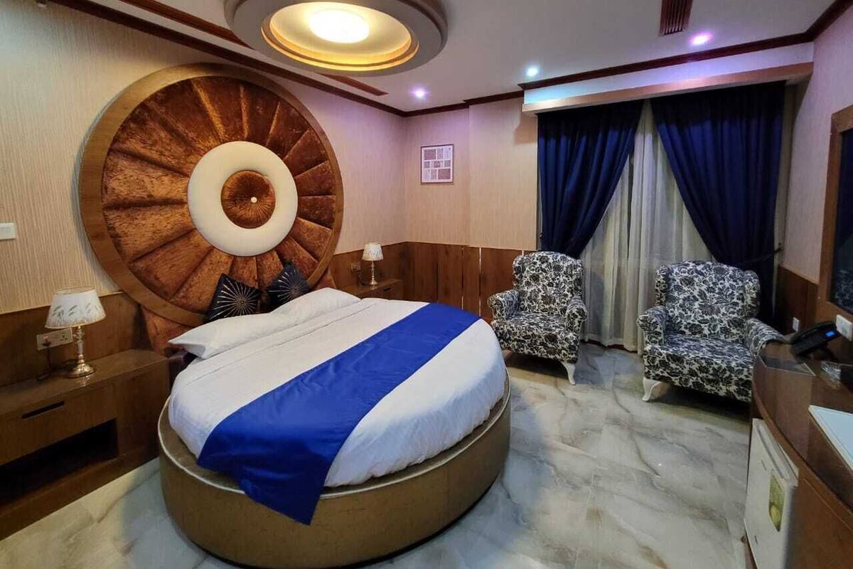 Una camera da letto con un letto rotondo, due poltrone a fantasia, una scrivania con un telefono e una grande sveglia a muro.