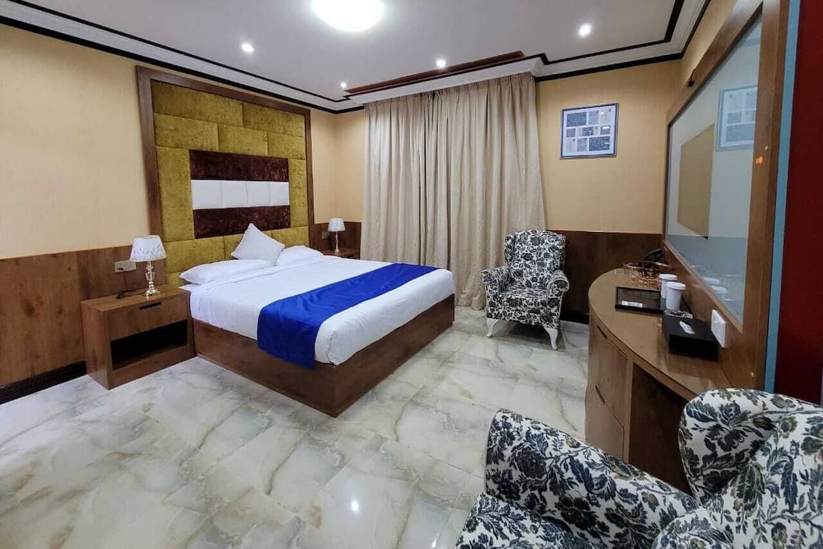 Una camera d'albergo con un letto grande, una scrivania con una sedia, una televisione e una finestra con tende.
