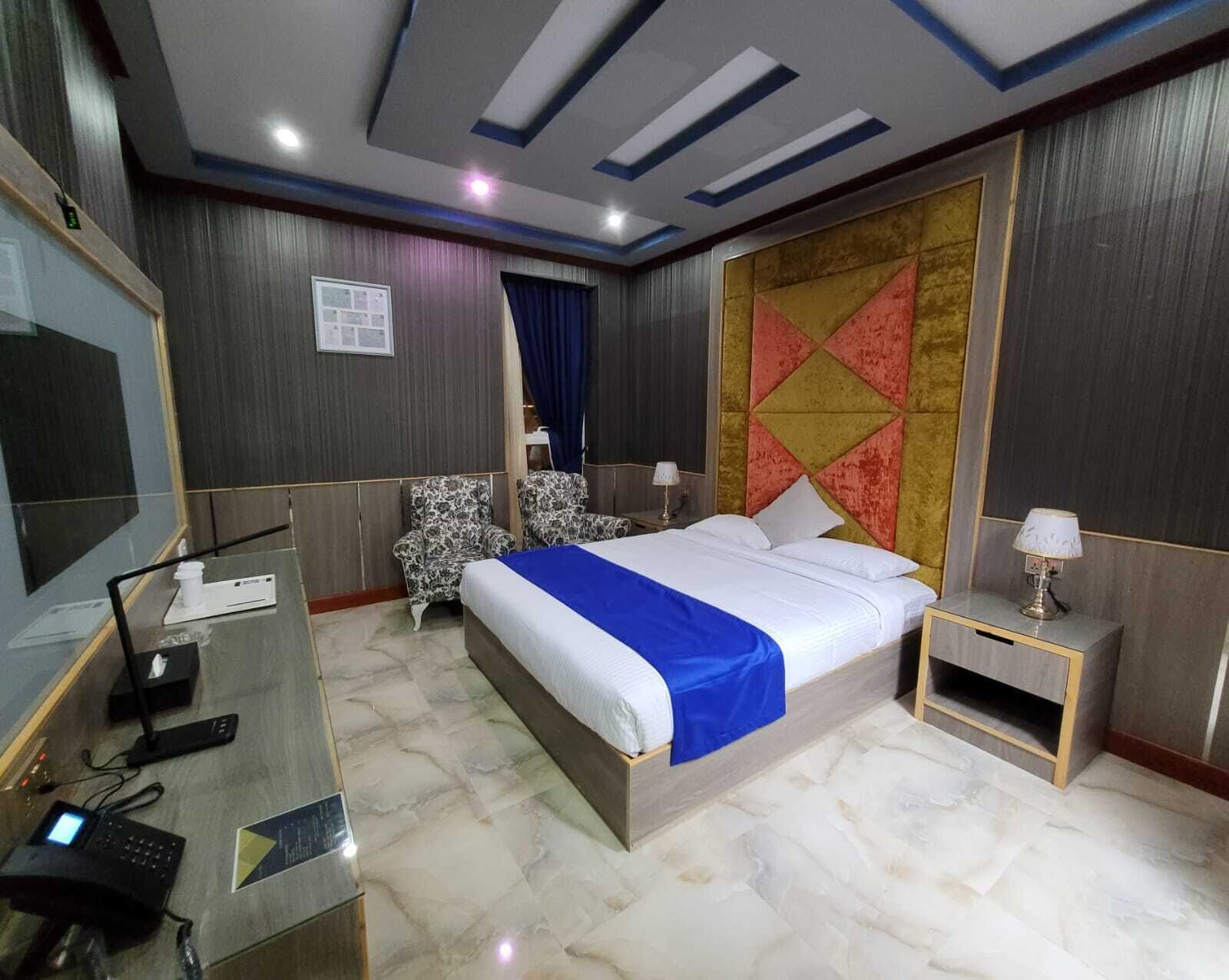 Une chambre d’hôtel avec un grand lit, un bureau avec un ordinateur, une télévision et un panneau décoratif au mur.