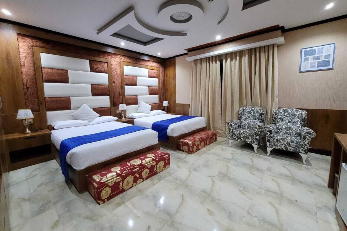 Camera d'albergo con due letti, una testiera in legno, pavimento in marmo e una poltrona con motivo decorativo, oltre a un tavolino.