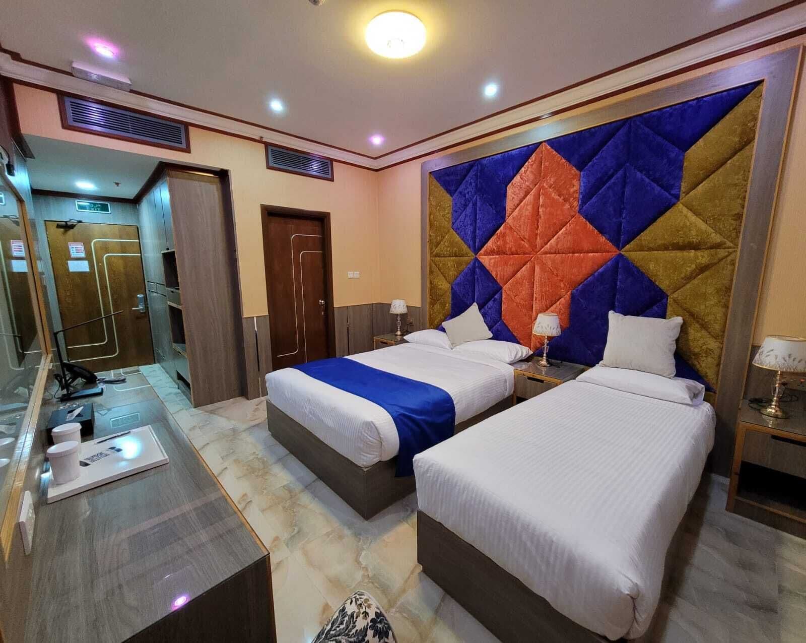 Une chambre d’hôtel avec deux lits, un sol en marbre, un grand panneau décoratif au mur et un miroir.