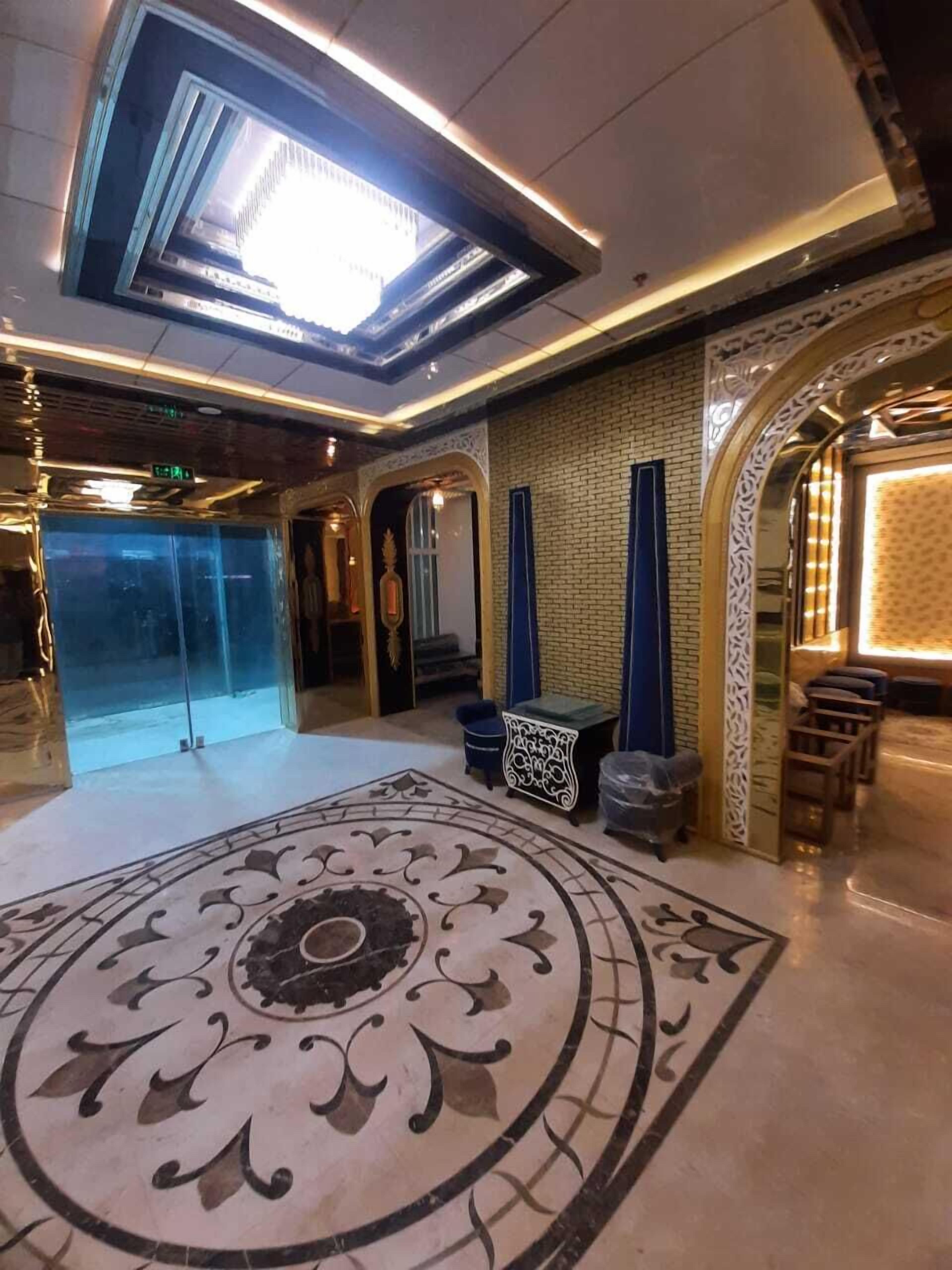 A lobby with a large decorative carpet, a glass door entrance, and a seating area with blue chairs.