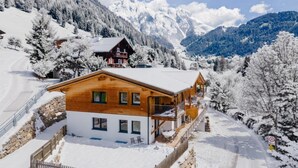 Un chalet en bois doté d’un balcon, entouré de montagnes et d’arbres couverts de neige.