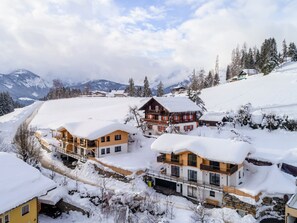 Vila montanhosa coberta de neve com casas de madeira tradicionais, um teleférico de esqui e uma vista clara das montanhas ao redor.