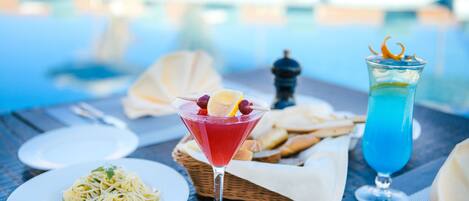 A dining table with a plate of spaghetti, a martini glass with a red drink, and a tall glass with a blue drink.
