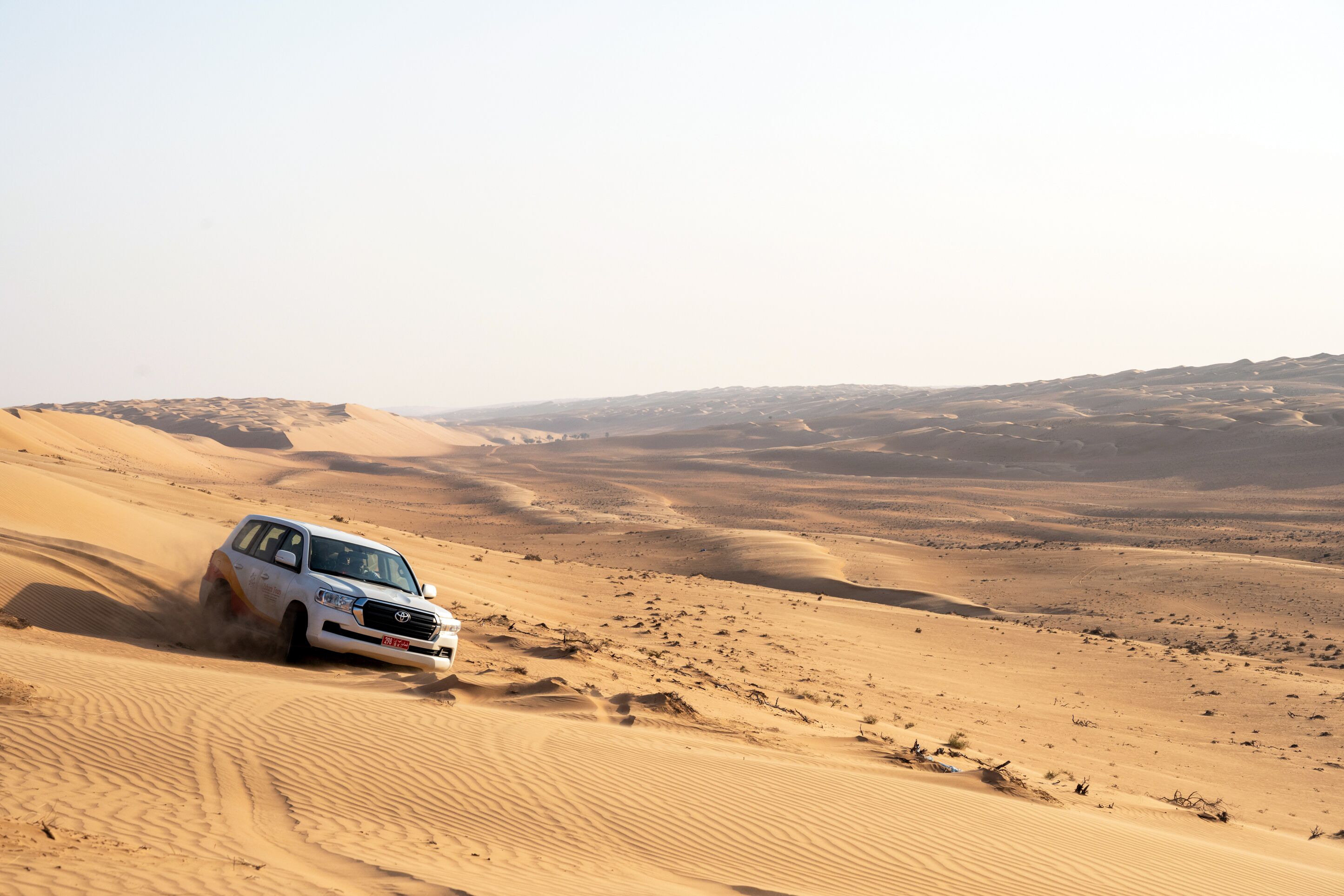 A white SUV driving through a desert landscape with sand dunes.