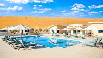 Un área de piscina con sillones de descanso y sombrillas, rodeada de colinas desérticas.