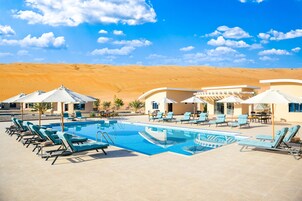 Un área de piscina con sillones de descanso y sombrillas, rodeada de colinas desérticas.