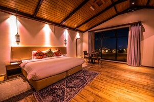 Un dormitorio espacioso con una cama grande, piso de madera y vistas al cielo nocturno a través de un ventanal.