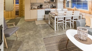 Une cuisine chaleureuse, aménagée dans un style rustique, avec des meubles en bois, un coin repas doté de chaises blanches et une grande fenêtre offrant une vue agréable.