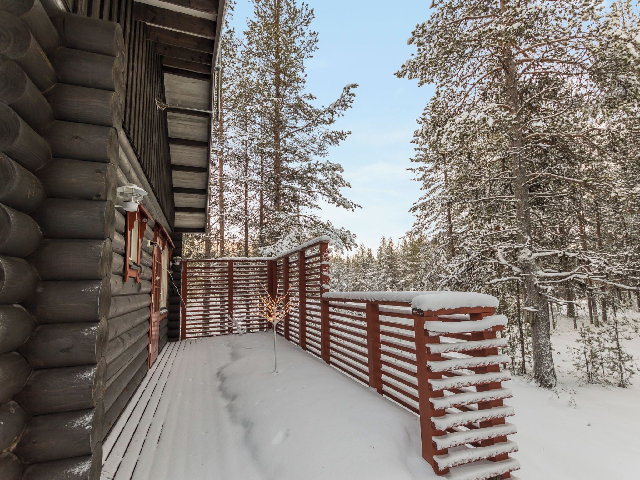 Une cabane en bois dotée d’une terrasse recouverte de neige et d’une balustrade en bois.