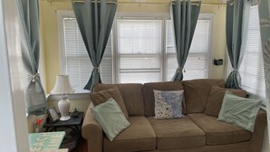 A cozy living room with a brown sofa, two pillows, a small table with a lamp, and a framed picture on the wall. - OCEAN BLOCK Downtown Rehoboth Beach 2BR Condo Sleeps 6 (Rehoboth Beach)