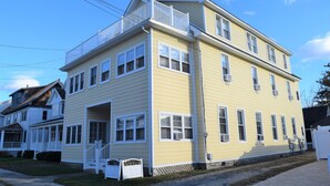 A two-story yellow building with white trim, a balcony on the second floor, and a front porch with steps. - OCEAN BLOCK Downtown Rehoboth Beach 2BR Condo Sleeps 6 (Rehoboth Beach)