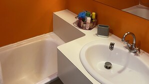A bathroom with a bathtub, a sink, and a mirror. There is a shelf with toiletries and a towel rack above the sink. - Coquet studio, heart of the resort, sleeps 4, south-west facing (Bourg-Saint-Maurice)