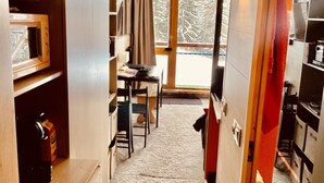 A compact kitchen with a microwave, a small table, and a chair. There is a door leading to a balcony with a view of trees. - Coquet studio, heart of the resort, sleeps 4, south-west facing (Bourg-Saint-Maurice)