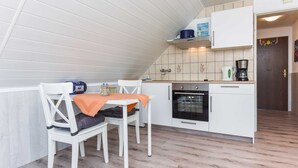 Cozinha compacta com armários brancos, uma pequena área de refeições com duas cadeiras e piso de madeira.