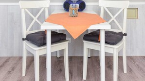Um espaço de refeições pequeno com uma mesa branca e duas cadeiras brancas, um alto-falante azul e um objeto decorativo pequeno sobre a mesa.