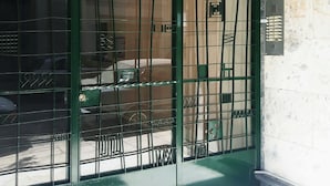 Un cancello di metallo verde con motivo a griglia, un muro bianco con una targa numerica e una piccola area esterna con un'auto e un tavolo.