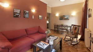 Een woonkamer met een rode bank, een salontafel met een tijdschrift, een vaas met bloemen, en een eethoek met een tafel en stoelen.