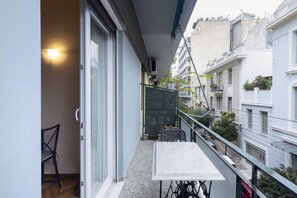 Un balcon avec une table et des chaises, une porte coulissante et une vue sur les immeubles voisins.