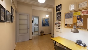 Een gang met een deur, een bureau met lamp, en diverse ingelijste foto's en berichten op de muren.